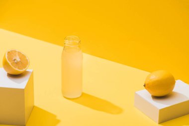 fresh juice in bottle near lemons and white cubes on yellow background