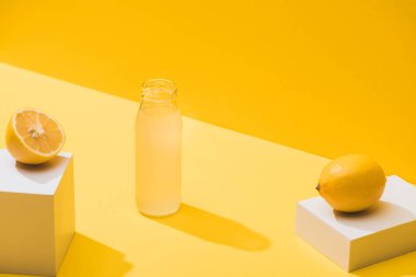fresh juice in bottle near lemons and white cubes on yellow background clipart