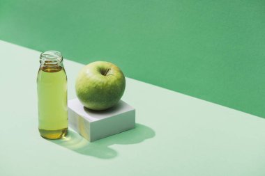 fresh juice near apple and and white cube on green and turquoise background