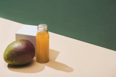 fresh juice in bottle near mango and white cube on green background