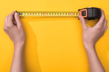 Top view of man holding industrial measuring tape on yellow background clipart