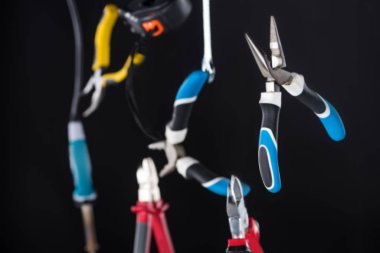 Selective focus of pliers and tools levitating in air isolated on black clipart