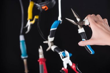 Cropped view of man holding pliers with levitating in air tools isolated on black clipart