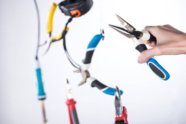Cropped view of man holding pliers with levitating tools in air isolated on grey clipart