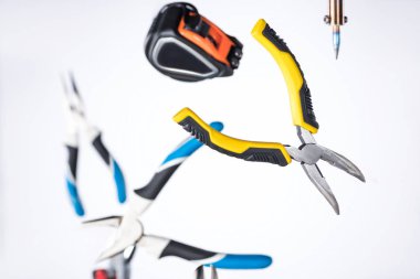 Selective focus of pliers, soldering iron and measuring tape levitating in air isolated on white clipart