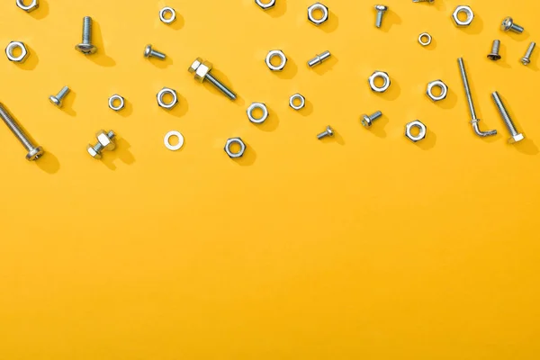コピースペースと黄色の背景に金属ナットとボルトのトップビュー — ストック写真