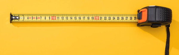 Top view of industrial measuring tape on yellow background, panoramic shot