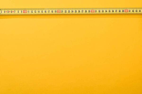 Top view of numbers on industrial measuring tape on yellow background