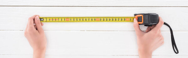 Top view of man holding industrial measuring tape on white wooden background, panoramic shot