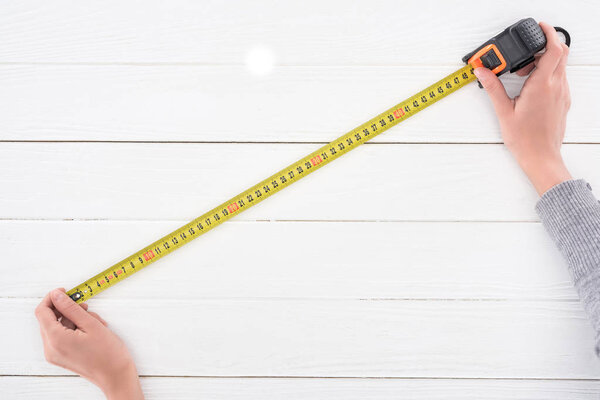 Cropped view of man holding industrial measuring tape on white wooden background