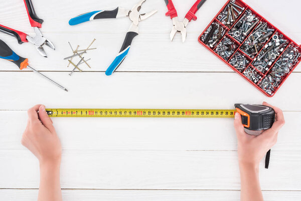 Вид сверху человека, держащего промышленную ленту рядом с инструментами на белом деревянном фоне
