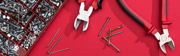 Top view of tool box with pliers and nails on red background, panoramic shot