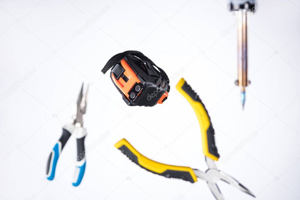 Selective focus of measuring tape with pliers and soldering iron levitating in air isolated on white