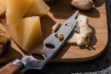 Selective focus of soft dorblu pressed by knife next to pieces of grana padano on cutting board clipart