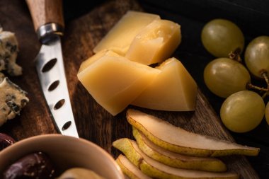 Grana Padano 'nun seçici odak noktası armut parçaları, bir kase zeytin, bıçak, dorblu, kesme tahtasındaki üzümler 