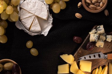 Camembert peyniri, üzümler, fındıklar, zeytinler, bıçaklı peynir, siyah arka planda armut.