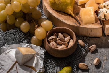 Üzüm, şam fıstığı ve gri arka planda Camembert peynirinin yanında ahşap tahtada armut olan peynir.
