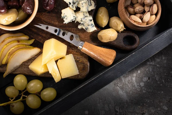 灰色の背景にチーズ 乾燥オリーブ ピスタチオ ブドウ ナイフのスライスでトレイのトップビュー — ストック写真