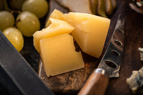 Selective focus of pieces of cheese and knife on cutting board next to grapes on tray