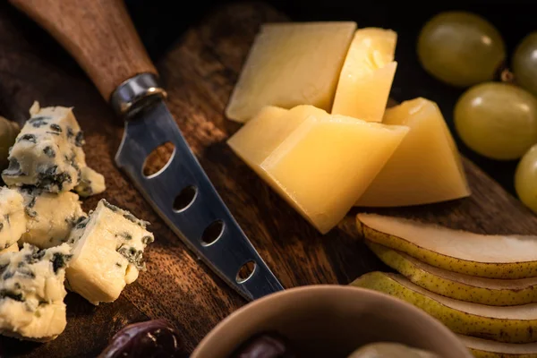 Selective focus of grana padano with bowl of olives, knife, slices of pear, grapes and dorblu on cutting board