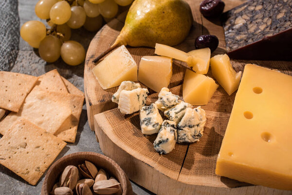 Selective focus of different kinds of cheese with pear and olives on wooden board next to grapes, nuts and crackers