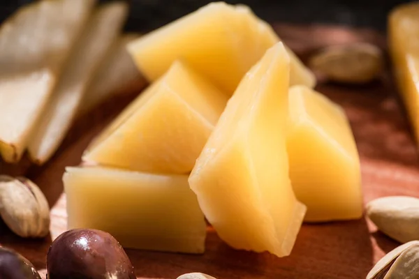 Selective focus of pieces of grana padano with olives, slices of pear and pistachios on wooden background