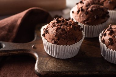 close up view of fresh chocolate muffins on wooden cutting board