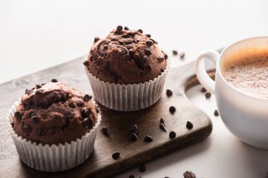 fresh chocolate muffins on wooden cutting board near cappuccino