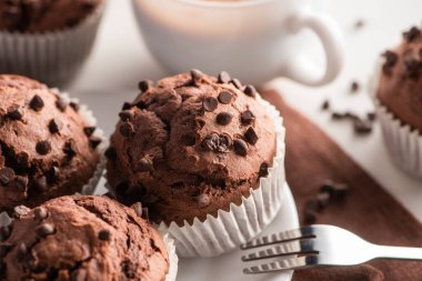 close up view of fresh chocolate muffins on white plate near fork