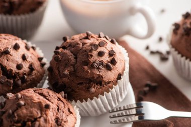 close up view of fresh chocolate muffins on white plate near fork clipart