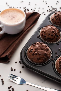 fresh chocolate muffins in muffin tin near brown napkin with coffee