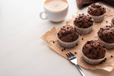 fresh chocolate muffins on parchment paper with fork near coffee
