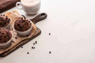 fresh chocolate muffins on wooden cutting board near coffee