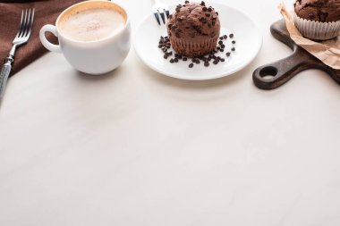 fresh chocolate muffins on wooden cutting board and plate with forks near coffee