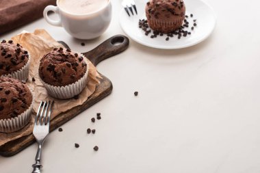 fresh chocolate muffins on wooden cutting board and plate with forks near coffee