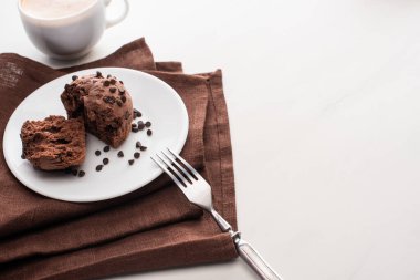 fresh chocolate muffins on plate with fork on brown napkin near coffee