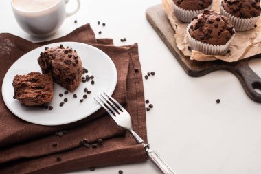 fresh chocolate muffins on wooden cutting board near plate with fork and coffee