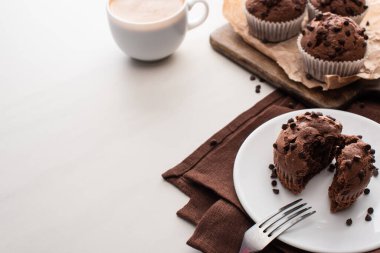fresh chocolate muffins on wooden cutting board near plate with fork and coffee