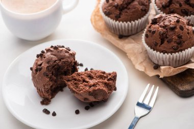 fresh chocolate muffins on wooden cutting board near plate, fork and coffee