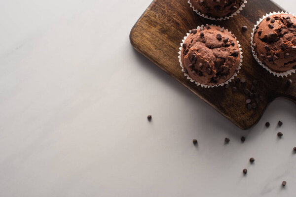 top view of fresh chocolate muffins on wooden cutting board on marble surface