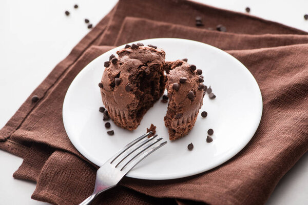Свежий шоколадный кекс на белой тарелке рядом с вилкой и салфеткой
