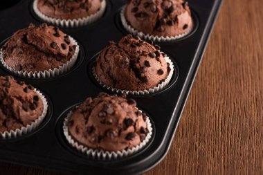 close up view of fresh chocolate muffins in muffin tin on wooden surface