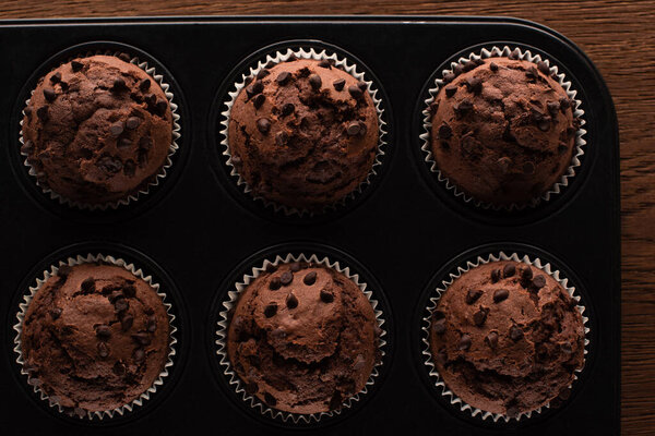 top view of fresh chocolate muffins in muffin tin on wooden surface