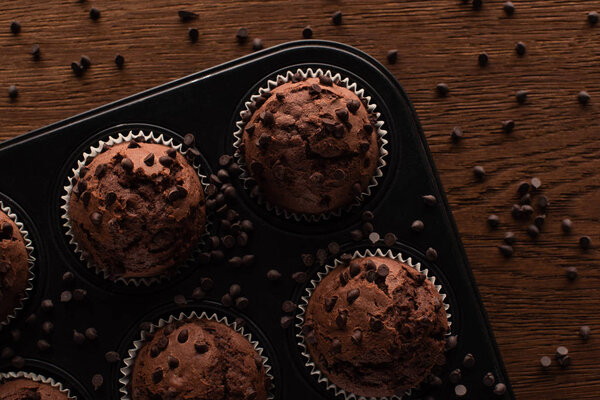 top view of fresh chocolate muffins in muffin tin on wooden surface