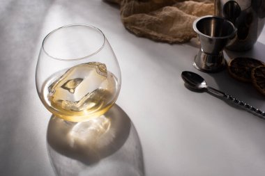 şeffaf cam buz küplü ve beyaz masada viski kumaş, kaşık ve jigger yanında gölge