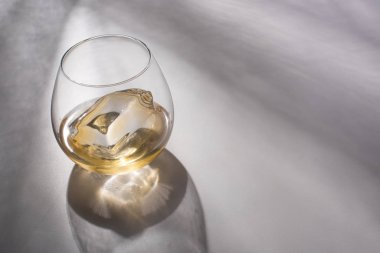 transparent glass with ice cube and whiskey on white table with shadow clipart