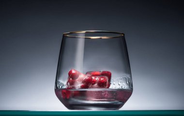 transparent glass with frozen redcurrant in ice cubes and vodka in dark with back light clipart