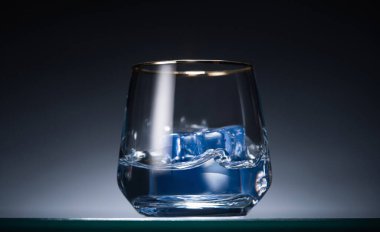 transparent glass with ice cubes and vodka in dark with blue back light clipart