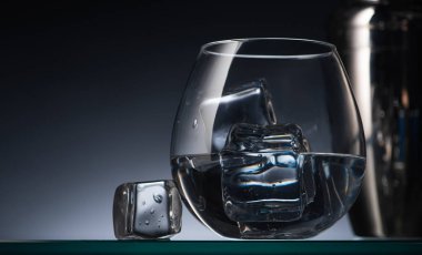 selective focus of transparent glass with ice cubes and vodka in dark with back light and shaker clipart