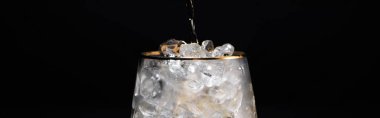 transparent glass with ice and pouring golden liquid isolated on black, panoramic shot clipart